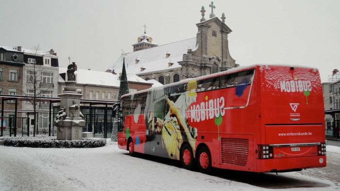 Roter Bus mit buntem Autoaufkleber, individuell gestaltbar, auf schneebedecktem Platz bei Signalshop.de.