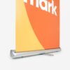 Roll-up-Banner mit orangefarbenem und gelbem Design, auf dem teilweise das Wort „Mark“ zu sehen ist.