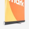 Nahaufnahme eines Roll-up-Banners mit einem Teil des Wortes „Mark“ auf orangefarbenem und gelbem Hintergrund.