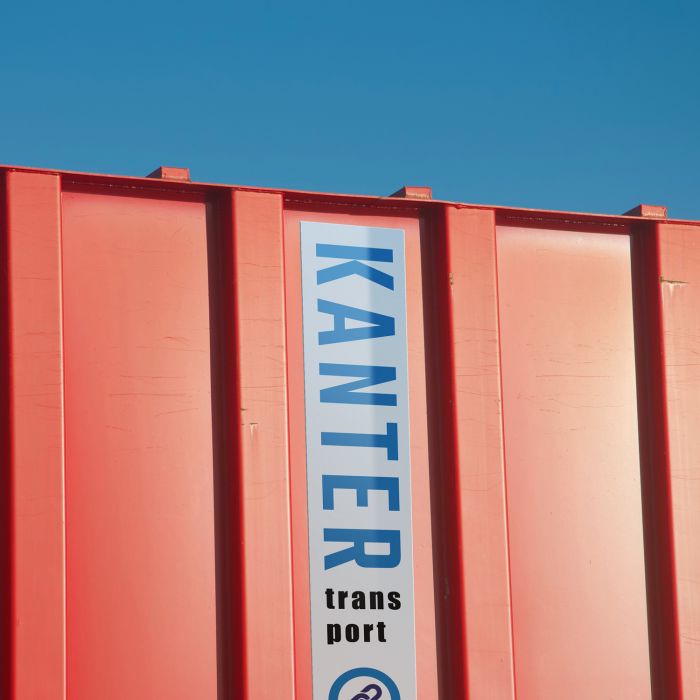 Roter Versandcontainer mit der Aufschrift „KANTER Transport“ auf der Seite, vor einem klaren blauen Himmel.