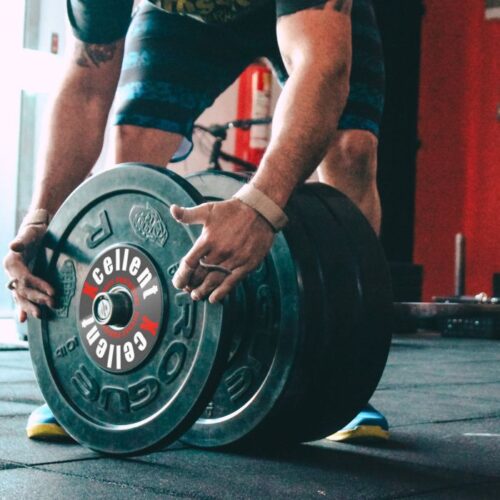 Person, die im Fitnessstudio schwere Hantelscheiben positioniert.