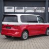 Der VW Bus mit der Bicolor-Folierung in rot und weiß steht mit geschlossenen Garagentoren vor einem Gebäude.