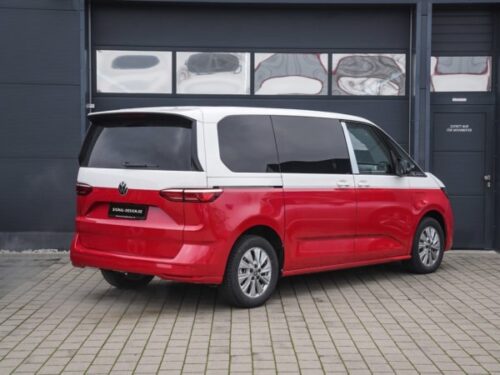 Der VW Bus mit der Bicolor-Folierung in rot und weiß steht mit geschlossenen Garagentoren vor einem Gebäude.