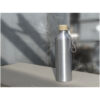 Wasserflasche aus Edelstahl mit Holzdeckel und Riemen, platziert auf einer Oberfläche mit unscharfem Außenhintergrund.