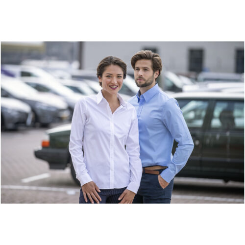 Eine Frau und ein Mann in formellen Hemden stehen lächelnd auf einem Parkplatz. Im Hintergrund sind Autos zu sehen.