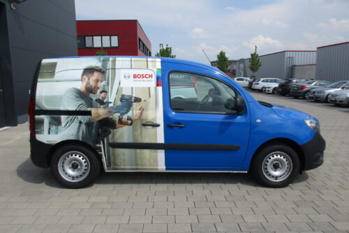 Blauer Bosch-Transporter mit Gestaltungskonzept Premium 699 €, vor den Fabriken geparkt.