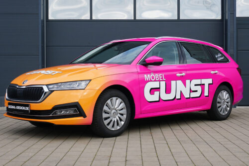 Pink-orangefarbenes Auto mit „Gestaltungskonzept Premium 699€“ auf befestigtem Untergrund.